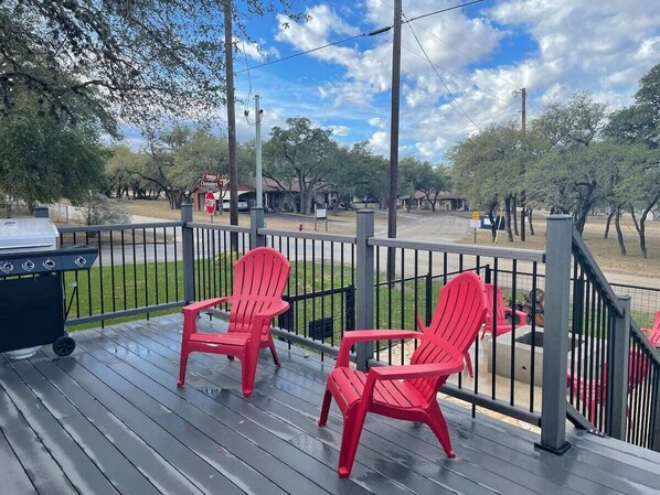 Une terrasse en bois avec des fauteuils Adirondack rouges, un barbecue et, au fond, un panneau de signalisation.
