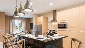 A modern kitchen with a central island, wooden cabinets, stainless steel appliances, and a dining area with chairs and a table set for six. - Near Disney, Resort Style, Free Parking & Wi-Fi Outdoor Pool (Kissimmee)