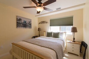 Ein Schlafzimmer mit Bett, Nachttischen, Deckenventilator, Fenster mit Jalousien und Stadtbildgemälde an der Wand.