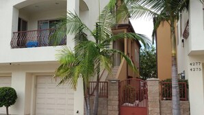 A two-story residential building with a garage, a gated entrance, and a small tree in the front yard. - Beautiful By the Beach/King bed/AC/2 car garage (San Diego)