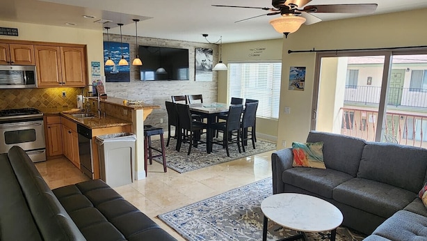 A modern kitchen with wooden cabinets, a dining area with a table and chairs, a gray sofa, and a ceiling fan. - Beautiful By the Beach/King bed/AC/2 car garage (San Diego)