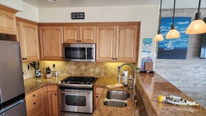 A kitchen with wooden cabinets, stainless steel appliances, a granite countertop, and a view of the beach through the window. - Beautiful By the Beach/King bed/AC/2 car garage (San Diego)