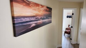A hallway with a large painting of a sunset over the ocean, a wooden floor, and a door leading to another room. - Beautiful By the Beach/King bed/AC/2 car garage (San Diego)