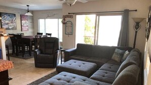 Ein Wohnzimmer mit einer Eckcouch, Poufs, einem Couchtisch und einem Essbereich mit Stühlen und einem Tisch.