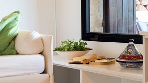 Un sofá blanco con un cojín verde, un cuenco blanco con plantas verdes y un recipiente cerámico decorativo sobre una estantería blanca.