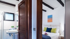 Un dormitorio con una cama, una mesita de noche y un buró. Se ve una ventana con vistas al exterior.