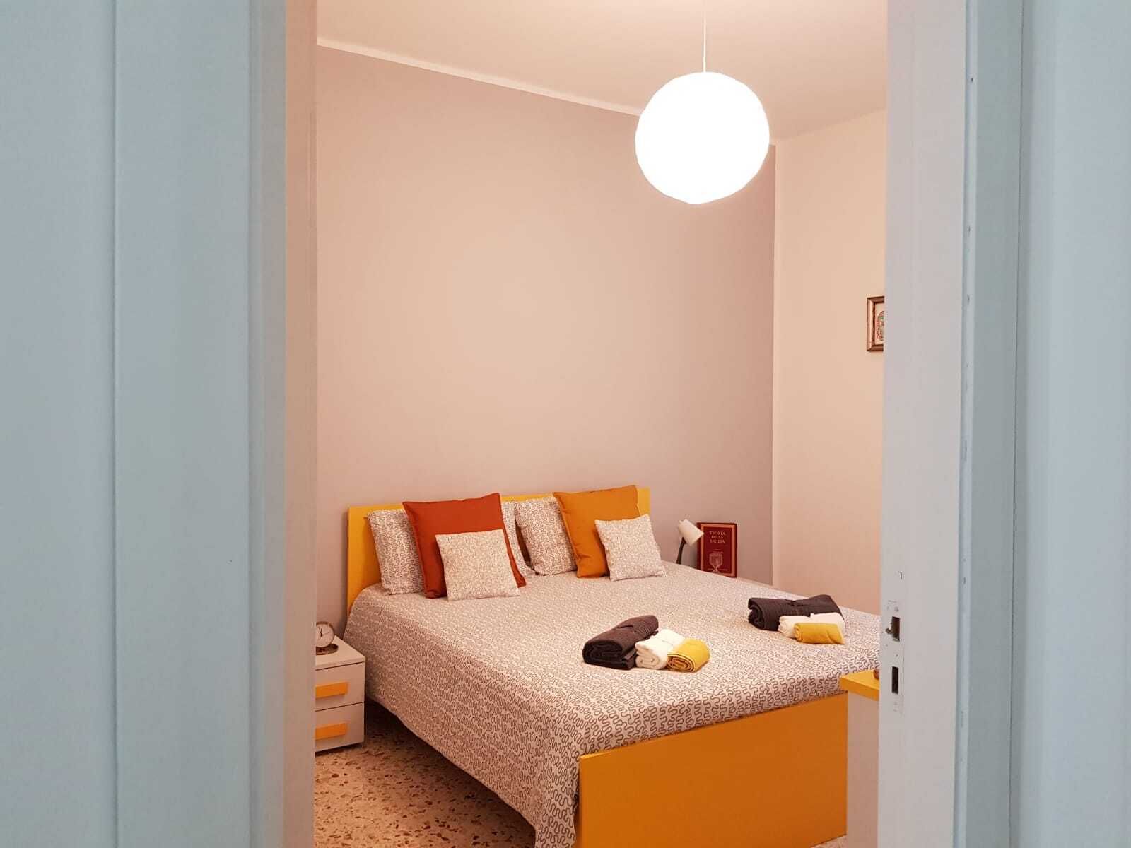 Een kleine slaapkamer met een bed, nachtkastje en een hanglamp.