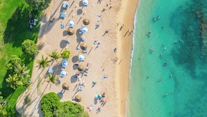 Une vue aérienne d’une plage avec des parasols, des palmiers et des personnes.