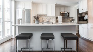 A modern kitchen with white cabinets, stainless steel appliances, and a large island with three bar stools.