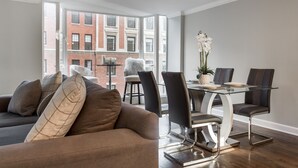 A modern living room with a glass dining table, dark leather chairs, and a brown sofa with patterned cushions.