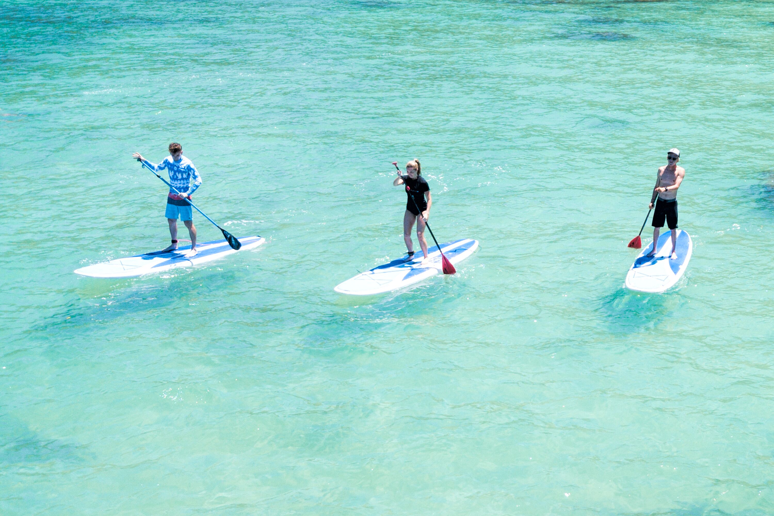 Tre personer står på paddleboards på et klart, blåt hav.