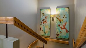 Un escalier avec des rampes en bois, une lucarne et deux œuvres d’art fixées au mur représentant des oiseaux et des fleurs.