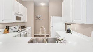 A modern kitchen with white cabinetry, a stainless steel sink, a built-in microwave, and a coffee maker. - 611 Lucaya (Davenport)