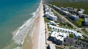 Vista aerea di una zona residenziale costiera con proprietà fronte spiaggia, tra cui edifici a più piani e una spiaggia.