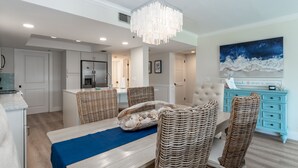 Una cucina moderna con frigorifero integrato, un'area pranzo con sedie in vimini e un tappeto blu, e un comò color acquamarina con oggetti decorativi.