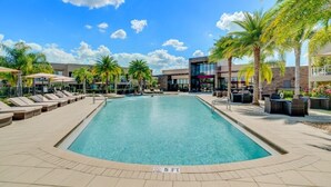A swimming pool with lounge chairs and palm trees, surrounded by a building with a modern design. - 3103brasilla (Kissimmee)