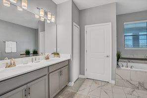 A modern bathroom with a double sink vanity, a large mirror, and a bathtub.