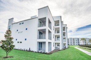 A modern multi-story building with balconies and a well-maintained lawn.