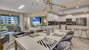 A modern kitchen with white cabinets, stainless steel appliances, and a dining area with striped placemats and a large table. - 3180paraunit101 (Kissimmee)