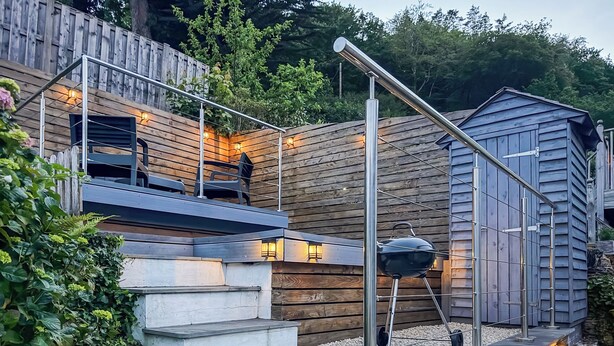 Una terrassa de fusta amb escales cap a una zona d'estar, un barbacoa i un cobert petit.