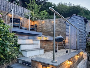 Une terrasse en bois avec des marches menant à un espace détente, un barbecue et un petit abri de jardin.