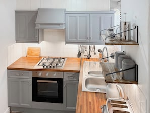 Une cuisine équipée d’une cuisinière à gaz, d’un four, d’un plan de travail en bois, de placards gris et d’un évier.