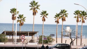 En strandpromenade med palmer, en overdækket siddeplads og udsigt over havet.