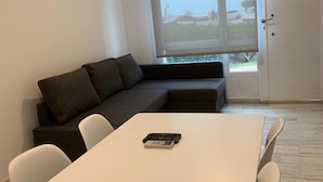 En moderne stue med et hvidt bord, en mørk sofa og et stort vindue med udsigt.