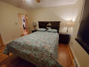 A bedroom with a floral bedspread, wooden headboard, two bedside tables with lamps, and a window with blinds. - Eagle's Nest by Table Rock. Perfect for Hickers, Cyclers, and Swimmers. (Sunset)