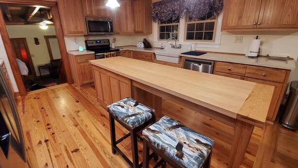 A kitchen with wooden cabinets, a microwave, a sink, and a large island with bar stools. - Eagle's Nest by Table Rock. Perfect for Hickers, Cyclers, and Swimmers. (Sunset)