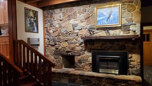 A stone fireplace with a mounted television, a wooden staircase, and a framed picture on the wall. - Eagle's Nest by Table Rock. Perfect for Hickers, Cyclers, and Swimmers. (Sunset)