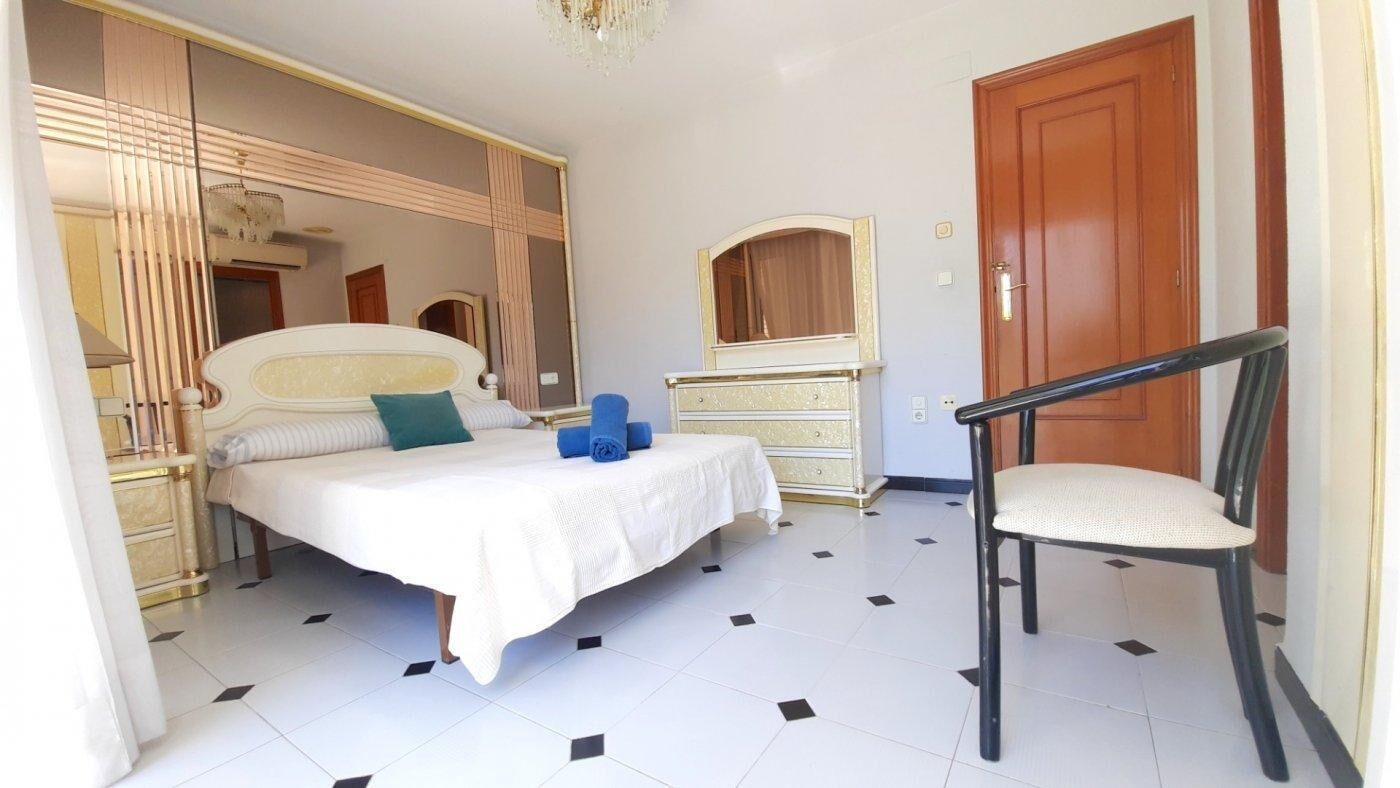 Un dormitorio con cama, una silla, un tocador y un espejo.