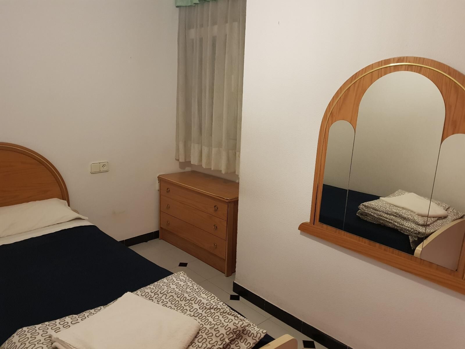 Un dormitorio con cama, cómoda, espejo y ventana con cortinas.