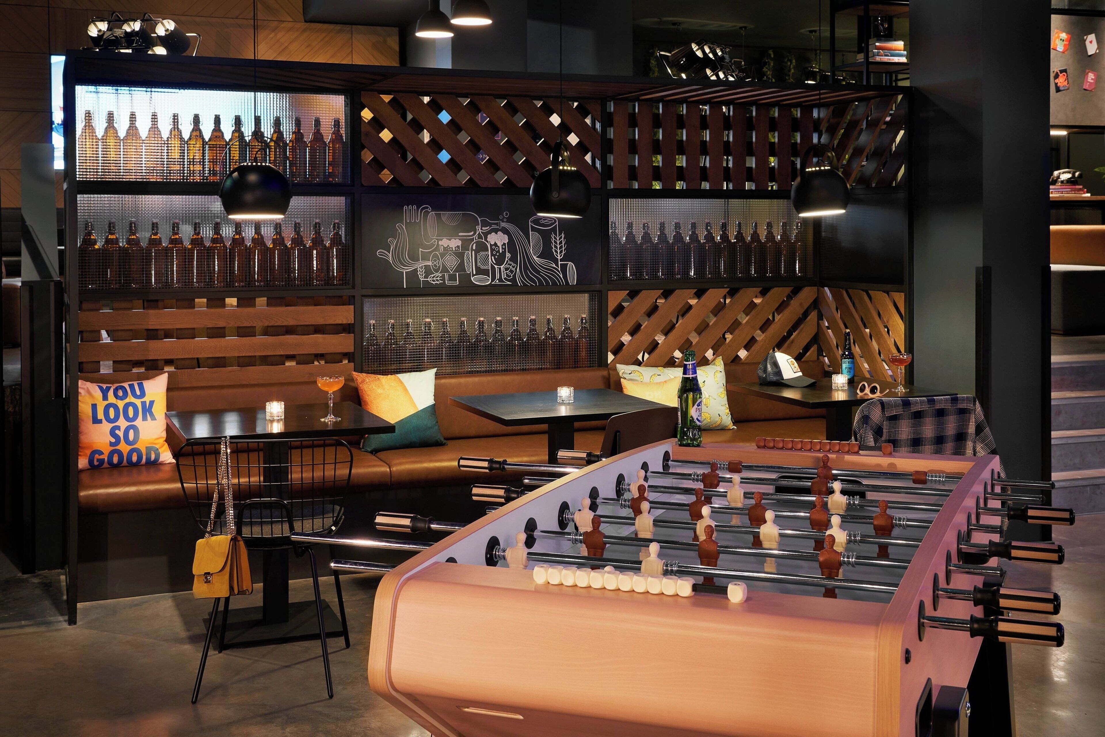 A bar area with a foosball table, seating, and a wall of liquor bottles.