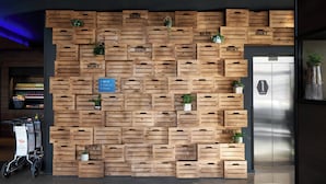 A wall with wooden crates labeled 'BEER' and 'MOXY', a sign indicating 'Meet Up' and 'Fitness' areas, and a refrigerator in the background. - Moxy Edinburgh (Edinburgh)