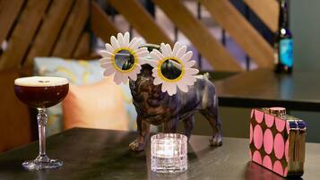 Een tafel met een glas rode wijn, een klein kaarsje, een decoratief hondje en een aansteker met roze en zwarte patronen.