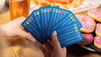 A person holding a deck of cards at a table with a pizza and a beer cup.