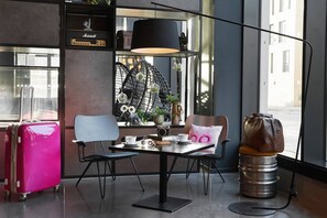 A modern cafe with a table, chairs, a vintage suitcase, and a unique seating option on a barrel. - Moxy Edinburgh (Edinburgh)