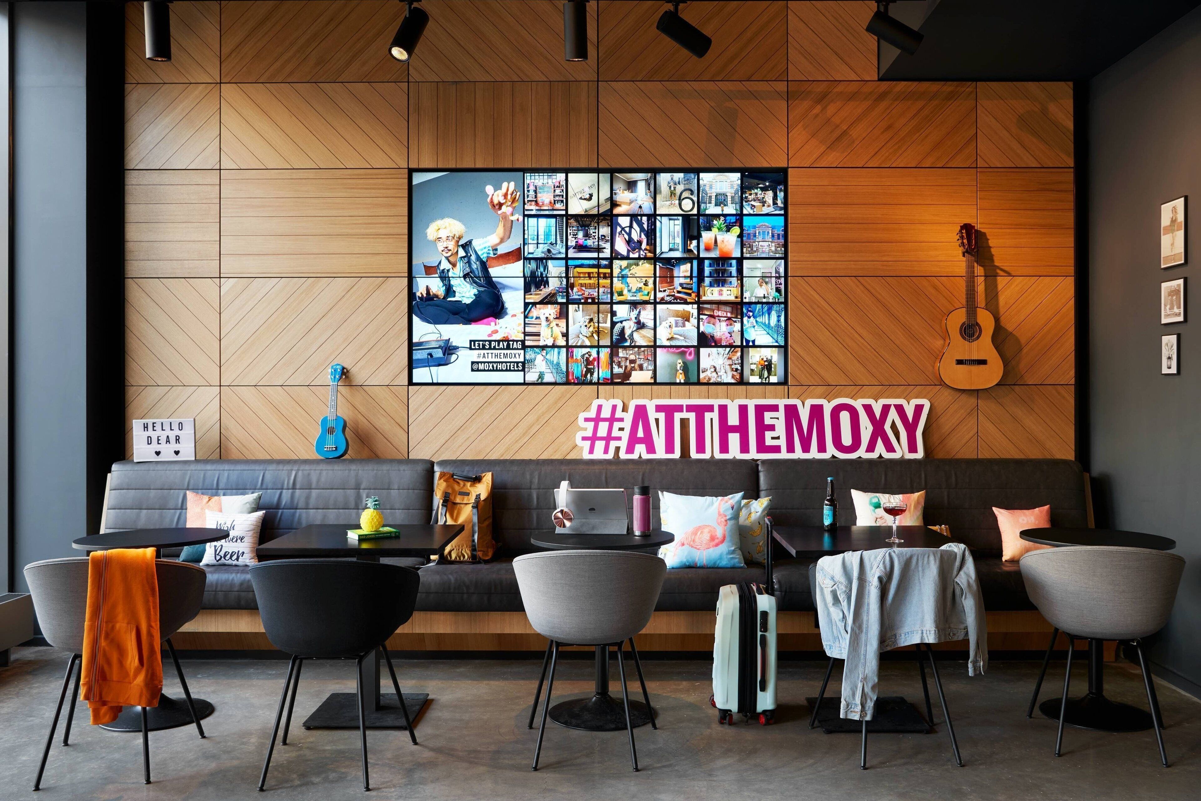 En moderne hotellobby med en trævæg, en stor fotocollage, en guitar, en sofa og et bord med en bærbar computer og et glas.