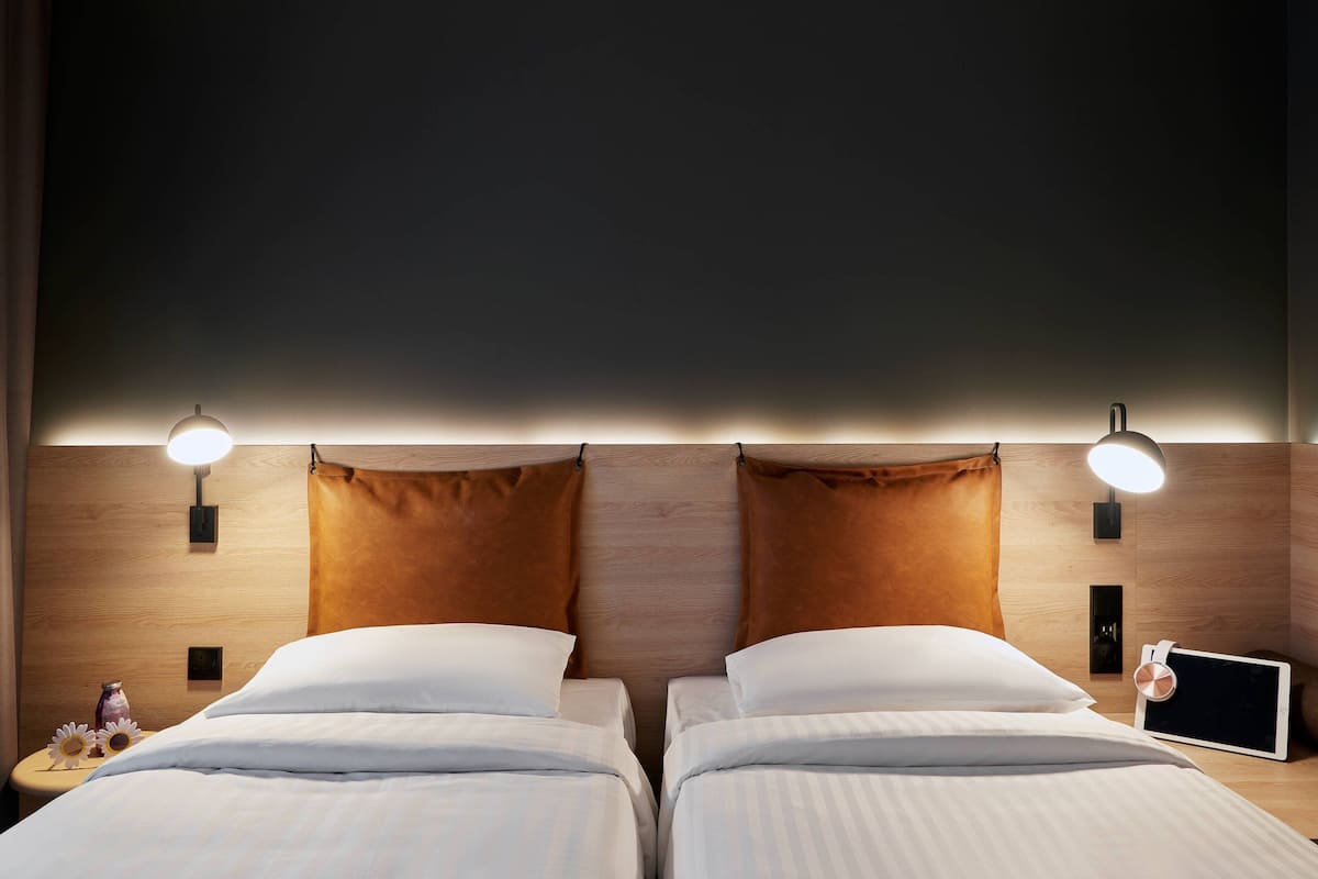 Un lit double avec du linge de lit blanc, deux lampes de chevet, une tablette sur la table de chevet et une tête de lit en bois.
