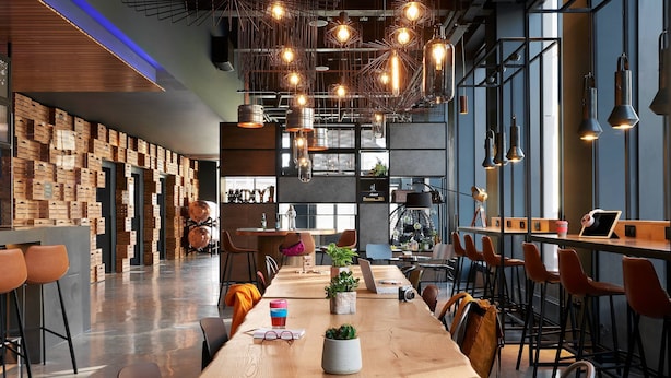 A modern bar area with wooden tables, bar stools, and hanging pendant lights. - Moxy Edinburgh (Edinburgh)