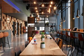 A modern bar area with wooden tables, bar stools, and hanging pendant lights. - Moxy Edinburgh (Edinburgh)