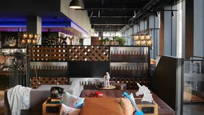 A modern lounge area with a sofa, a small table, and a bar area in the background. - Moxy Edinburgh (Edinburgh)