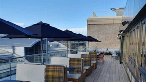 A wooden deck with outdoor seating and umbrellas, overlooking a cityscape. - Moxy Edinburgh (Edinburgh)