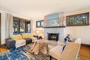 A living room with a fireplace, a sofa set, a coffee table, and large windows.