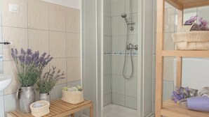 A modern bathroom with a glass-enclosed shower, wooden shelves, and a small table with toiletries. - Small house "BreadLady" (Koper)