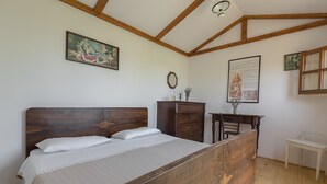 Ein Schlafzimmer mit einem hölzernen Bett, einem Schminktisch, einem Schreibtisch und einem Stuhl. An der Wand hängt ein Gemälde und es gibt ein gerahmtes Dokument.