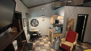A compact living space with a kitchen area, a dining table, a red armchair, and a television. - Enjoy the beautiful views of the Muskegon River near Hardy Dam and Dragon Trail (Newaygo)