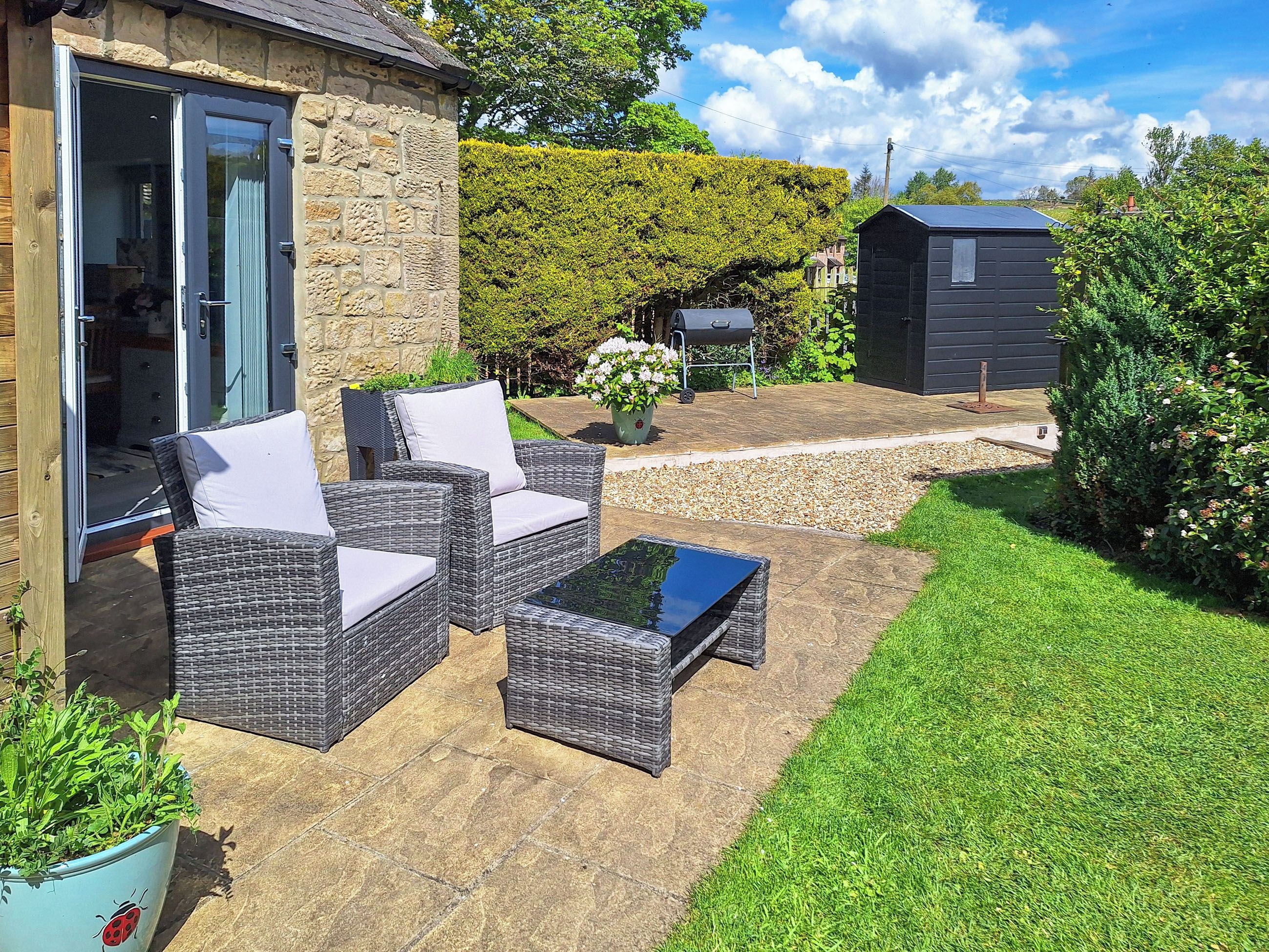 A patio with wicker furniture, a stone wall, and a garden.