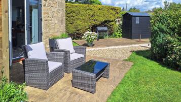 A patio with wicker furniture, a stone wall, and a garden.